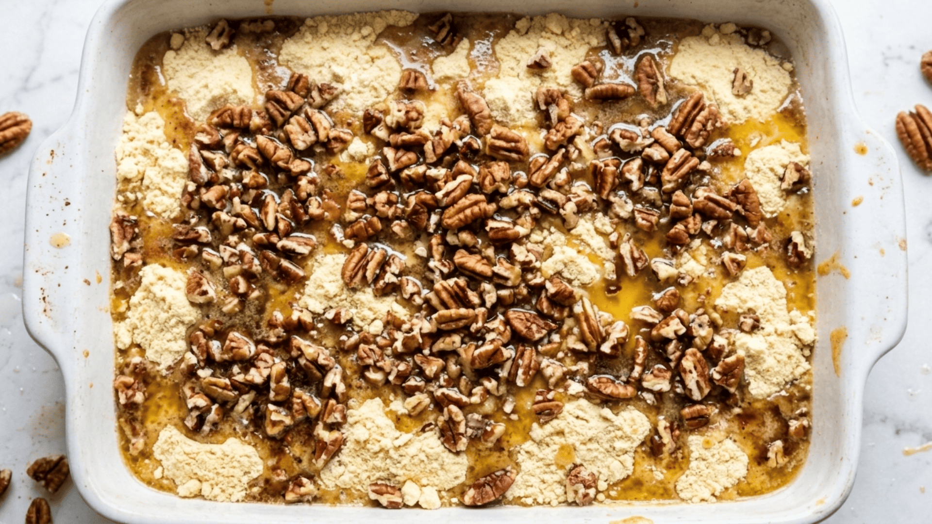 Melted butter being drizzled over cake mix and chopped pecans before baking