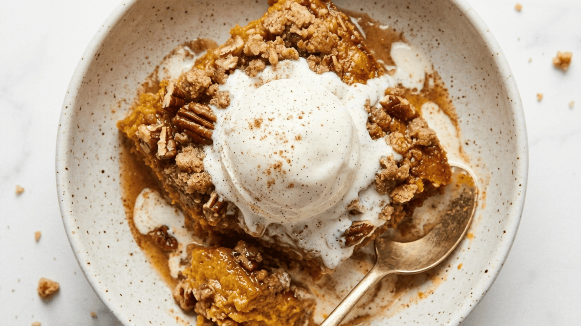 A serving of pumpkin dump cake on a plate showing the creamy pumpkin layer and crunchy buttery top, topped with a scoop of vanilla ice cream